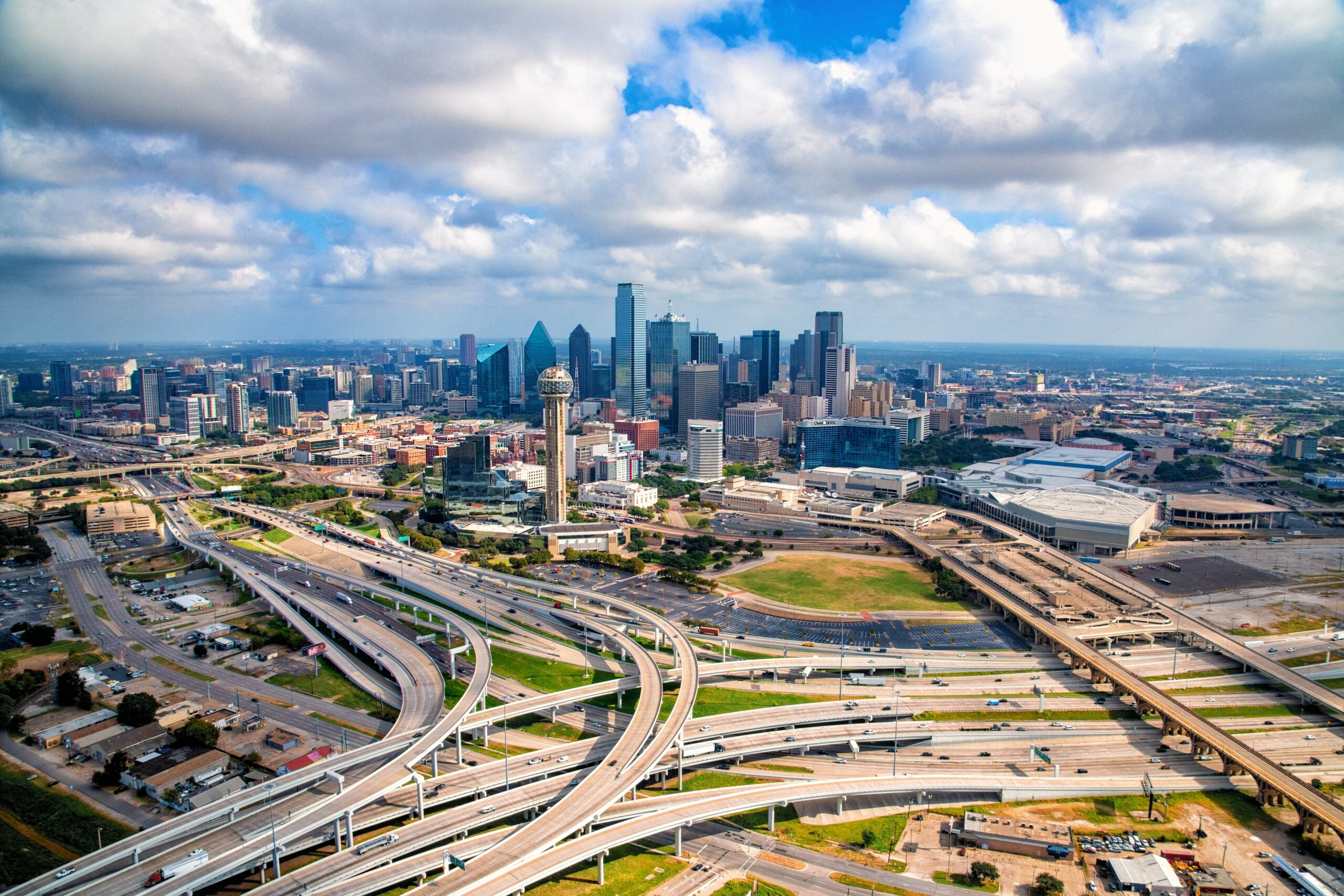 This is an aerial view of the spaghetti bowl-like highways leading into Dallas, skyscrapers standing tall in the background.
