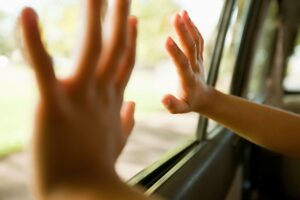 An infant is pictured here placing two hands on the inside of a car window. On average, 38 kids die every year of pediatric vehicular heatstroke.