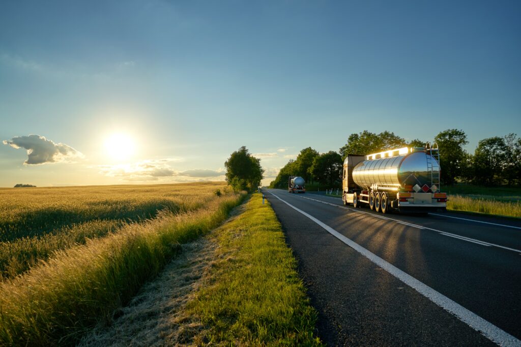 A couple of oil tankers are pictured heading west toward the sunset on a rural road.