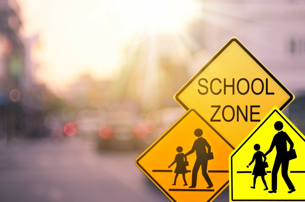This image depicts school zone signs in the foreground with blurred traffic in the background.