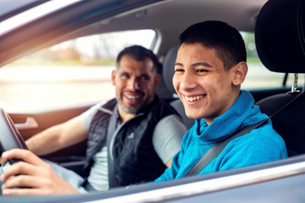 A teen driver is pictured working with his parent to learn safe driving habits.