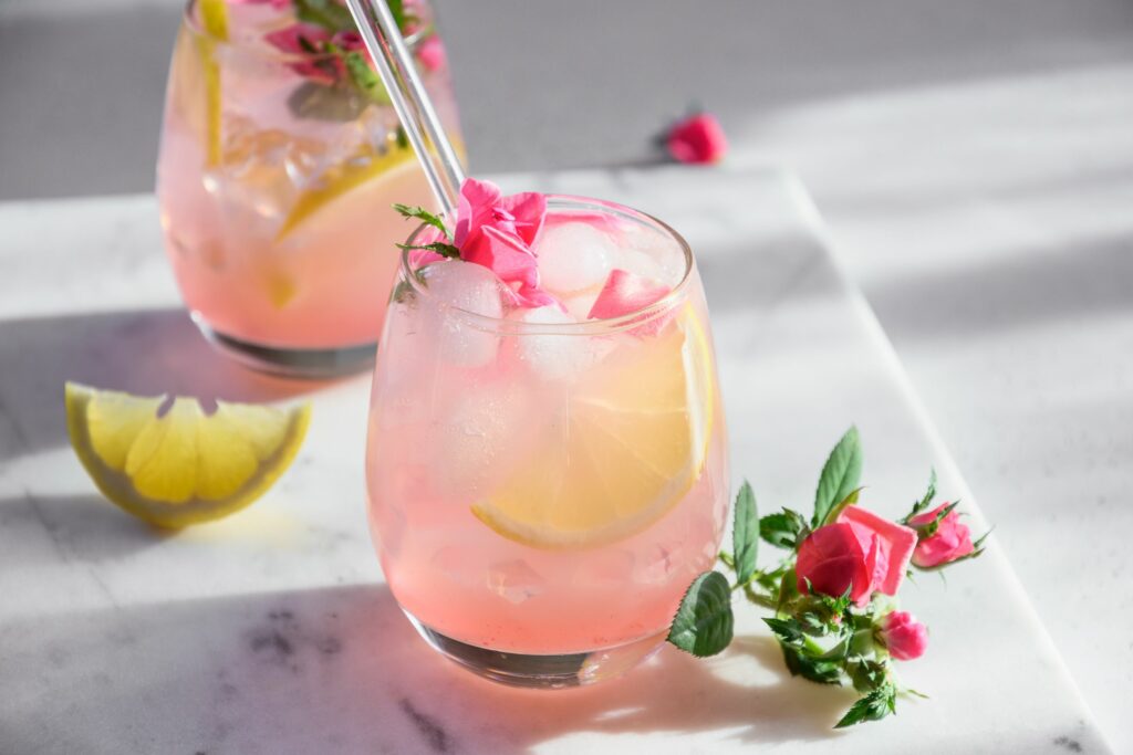 A glass of pink lemonade is pictured here with a fancy rose petal garnish.