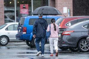 A couple walks through a parking lot under an umbrella on a rainy day.