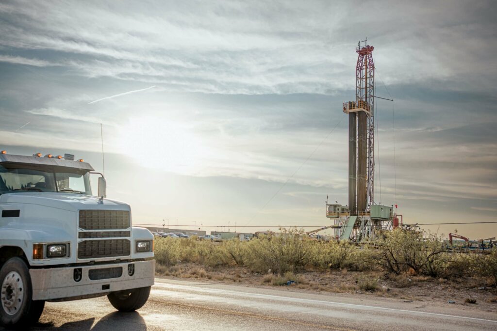 A truck is pictured here passing a drilling rig at dusk.