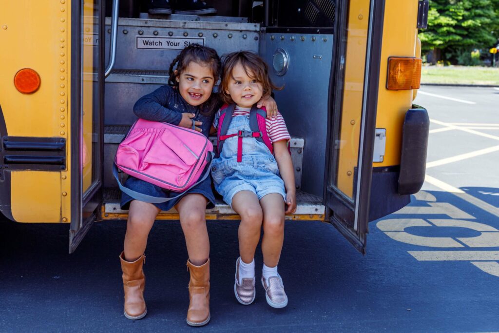 Two best friends pose for a photograph on the bus steps on the first day of school.