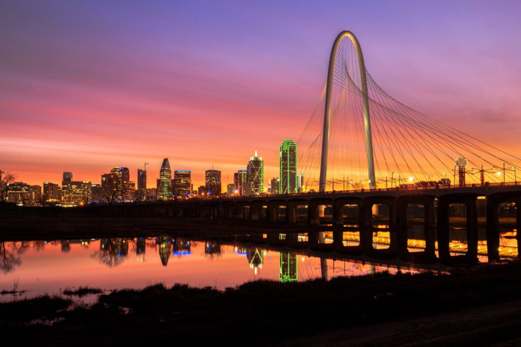 The sun rises here over the Margaret Hunt-Hill bridge in Dallas, the city skyline illuminated in the background.