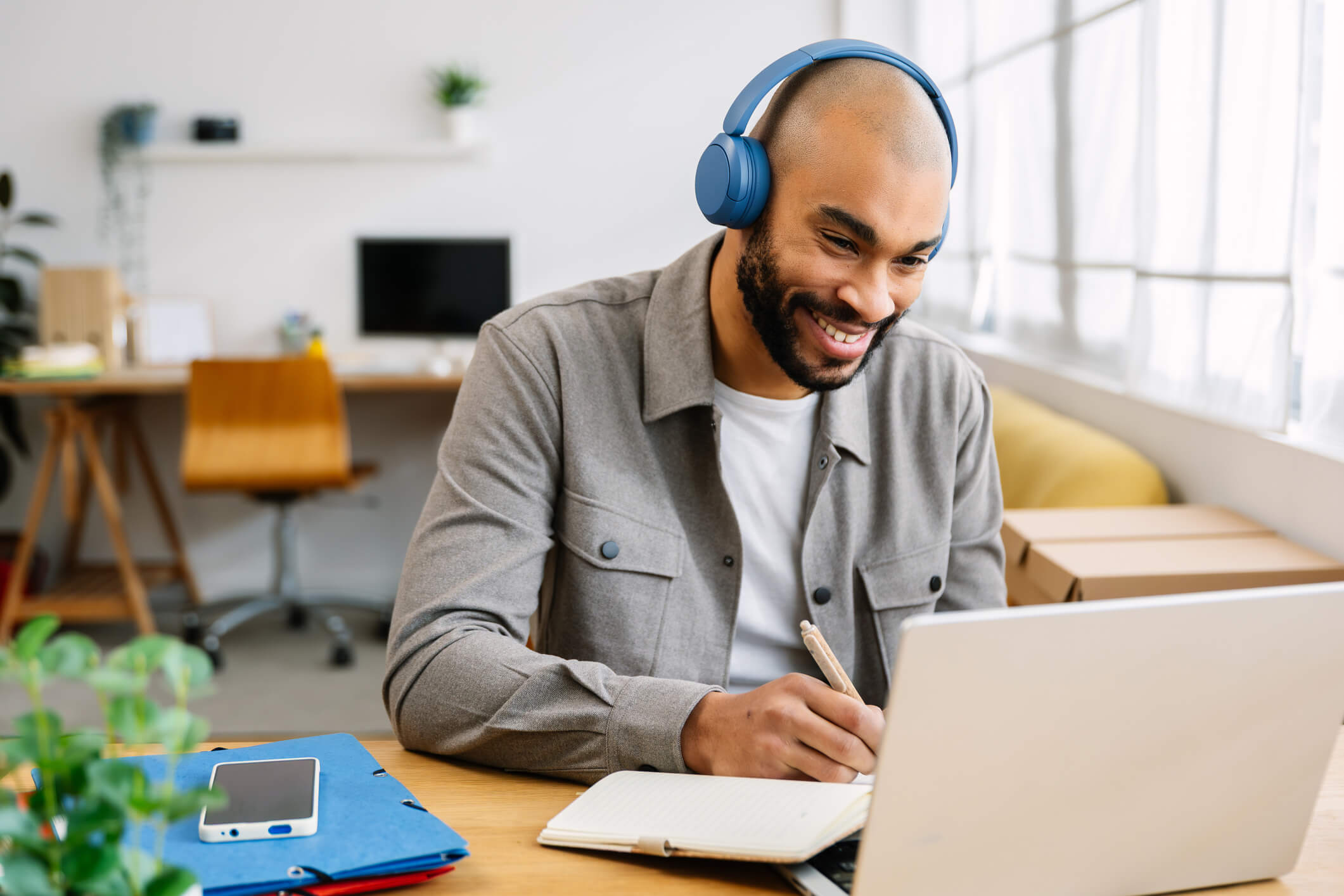A worker wearing headphones sits at a desk, his laptop open. He is completing an online training course.