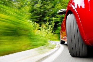 The front wheel on a bright, red vehicle is pictured here hugging the white line on a curve in the road.
